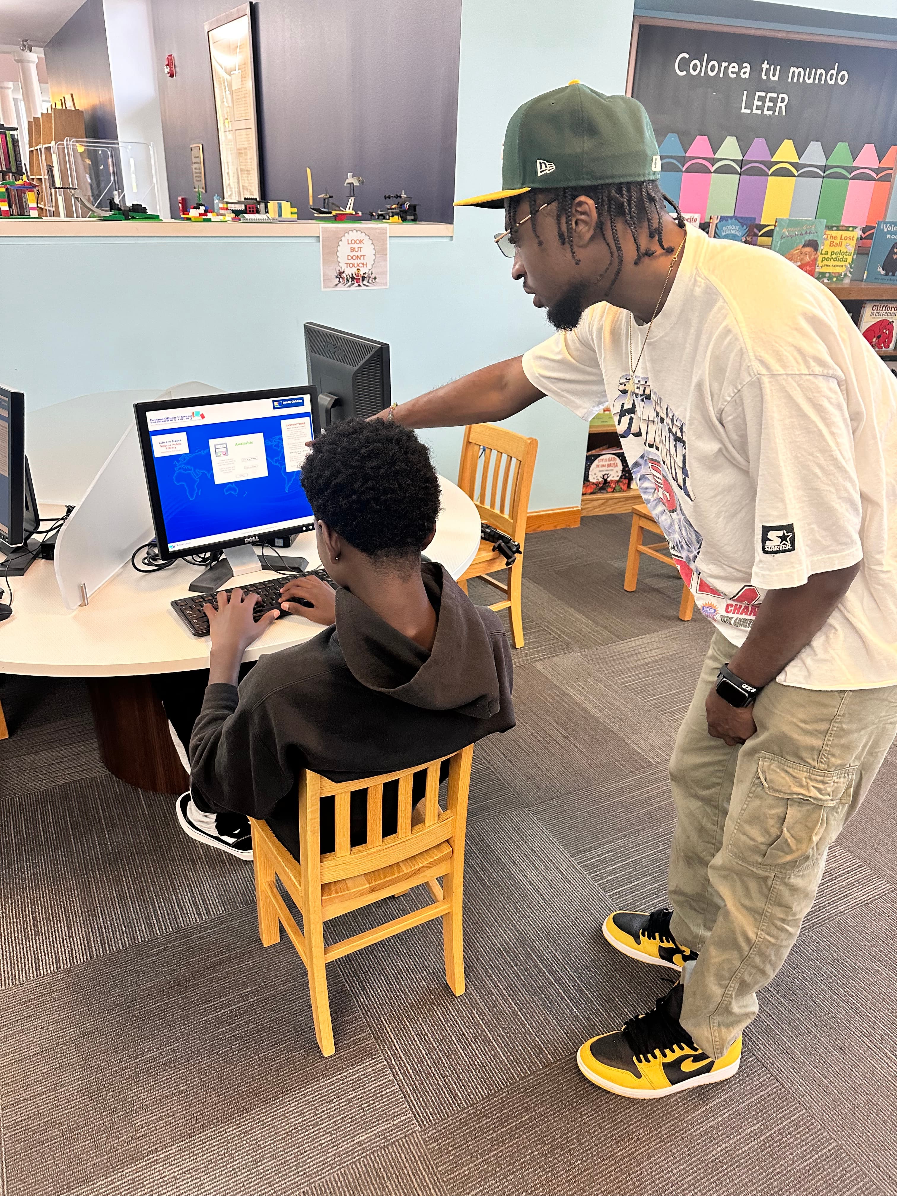 Jordan coaching a student at a library computer station.